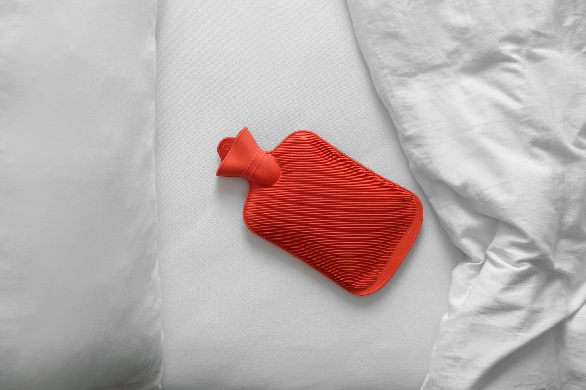 Rubber hot water bottle near soft blanket on bed, top view